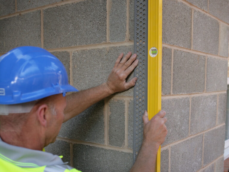Construction worker using spirit on vertical corner of block work to check level of PVCu render bead